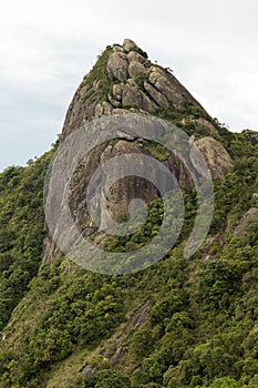 Vertical close up view of a mountain rock face with some trees under white cloudy - pico e serra do lopo photo