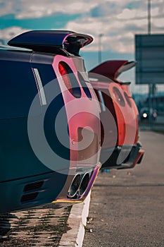 Vertical closeup of back parts of a red and purple racing cars with spoilers blurred sky background