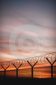 Vertical closeup of a barbed fence against the vivid sunset sky