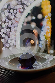 Vertical closeup of a chocolate bombshell with a unique swirled mirror glaze against blurred lights photo