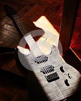 Vertical closeup of the electric guitar on wooden floor under sunlight