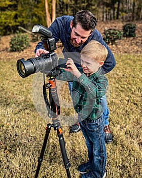Vertical closeup of a father teaching his son using a professional tripod camera outside