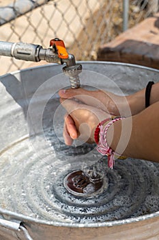 Vertical closeup of female washing hands outside, makeshift sink made of metal and pipes