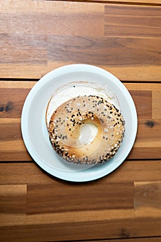 Vertical closeup of a fresh bagel with sesame and white sauce on a white plate