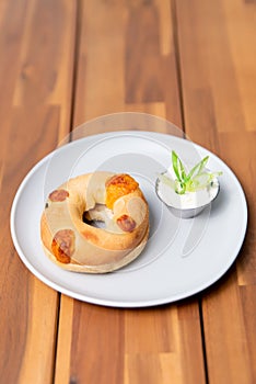 Vertical closeup of a fresh bagel and a white sauce in a small bowl isolated on a white plate