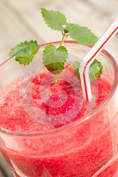 Vertical closeup of a glass of raspberry smoothie, with a plastic straw