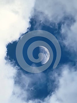 Vertical closeup of a half-moon in a daytime sky with clouds