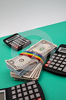 Vertical closeup of a pack of dollars tied with rainbow tape and black calculators around