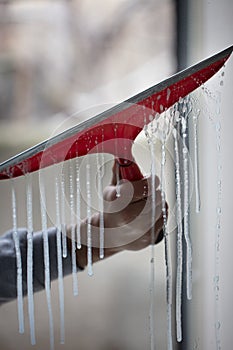 Vertical closeup of a person cleaning the window with a red squeegee