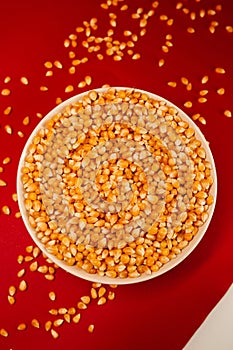 Vertical closeup of a popcorn bowl with some corns spilled around it isolated on a red background