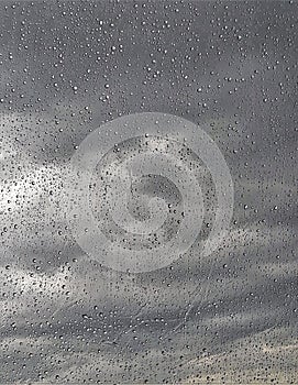 Vertical closeup of raindrops on the window with a cloudy sky on the blurry background