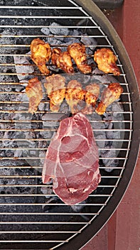 Vertical closeup of raw steak with fried chicken legs on the grill.