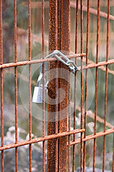 Vertical closeup of a rusty metal gate locked up with a chain and a lock
