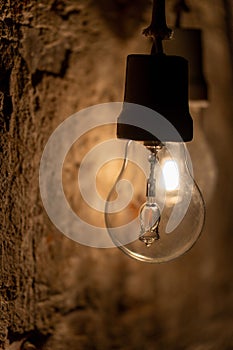 Vertical closeup shot of a bare light bulb hang on an old wall