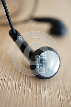 Vertical closeup shot of a black earphone on a wooden surface