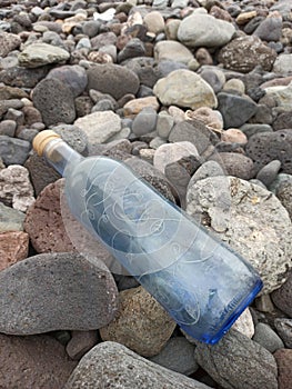 Vertical closeup shot of a blue water bottle with a note inside on the rocks by the beach