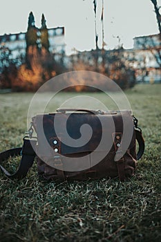 Vertical closeup shot of a brown leather satchel on the green grass