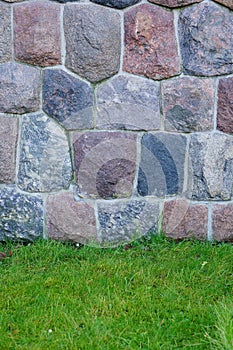 Vertical closeup shot of a cobblestone wall with colorful stones and the green grass below