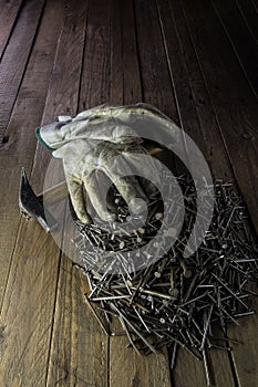 Vertical closeup shot of dirty white gloves, a hammer, and a stack of nails on the wooden ground