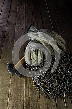 Vertical closeup shot of dirty white gloves on a hammer and a stack of nails on the wooden ground