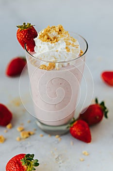 Vertical closeup shot of a glass of a strawberry milkshake surrounded by strawberries