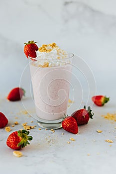 Vertical closeup shot of a glass of a strawberry milkshake surrounded by strawberries