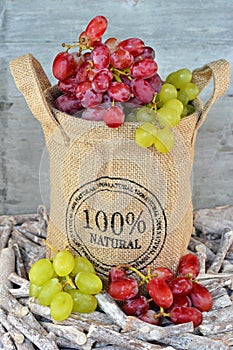 Vertical closeup shot of grapes in a burlap sack in twigs in front of a wooden background