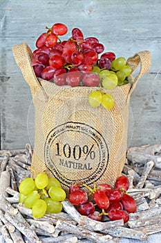 Vertical closeup shot of grapes in a burlap sack in twigs in front of a wooden background
