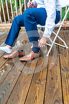 Vertical closeup shot of the groom putting on his brown shoes