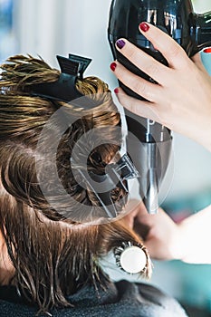 Vertical closeup shot of a hairdresser blow drying a woman's short hair in a beauty salon