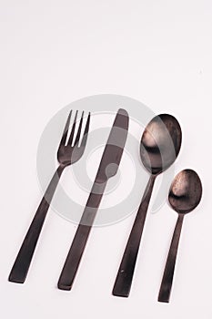 Vertical closeup shot of a knife, fork, and two spoons isolated on a light-colored background