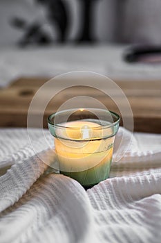 Vertical closeup shot of a litten candle on a white comforter and a wooden board in the background