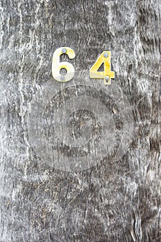 Vertical closeup shot of the number 64 attached to a tree trunk surface with screws