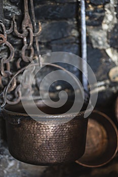 Vertical closeup shot of an old copper pot with rusty chains and aged brick wall in the background