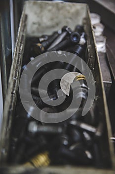 Vertical closeup shot of a pile of black tempered bolts in a metal box