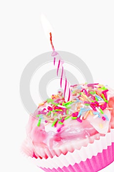 Vertical closeup shot of a pink cupcake with sprinkles and a candle