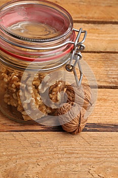 Vertical closeup shot of shelled walnuts in a glass jar and whole walnuts on a wooden table