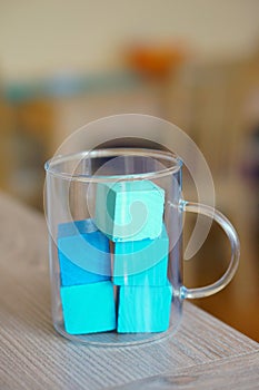 Vertical closeup shot of tea glass filled with blue wooden toy cubes standing on a table