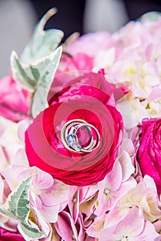 Vertical closeup shot of the wedding rings on the pink flower of the bride\'s bouquet