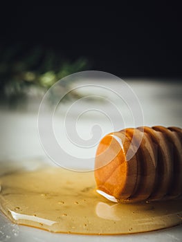 Vertical closeup shot of a wood dipper of honey and honey leaking from it on  a white surface