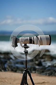 Vertical closeup of surf photography telephoto lens and camera body on tripod. Jeffreys Bay, Africa.