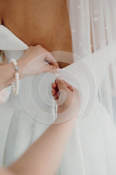 Vertical closeup of a woman carefully zipping up the bride& x27;s dress