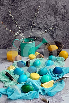 Vertical composition for Easter. Painted yellow, blue, green eggs on a napkin with macaroons and lemons on a light gray background