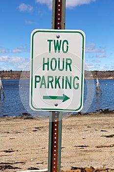 Vertical composition of an old two hour parking sign with a right arrow in front of a beach and ocean in the springtime in New