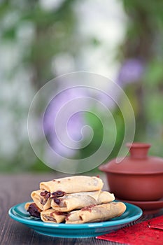 Vertical composition: a plate of spring rolls, a cup of tea and a red envelope.The Chinese character in the picture means `happine