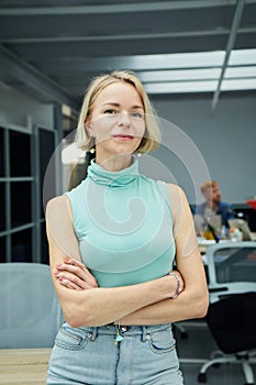 Vertical confident Caucasian business woman looking at camera standing with arms crossed in office.