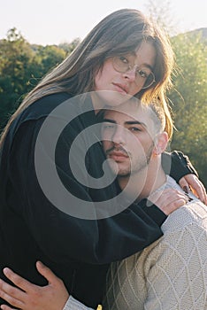 Vertical of a couple hugging each other and looking at the camera female standing higher