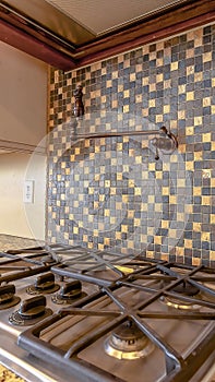 Vertical crop Cooktop under an exhaust hood and faucet mounted on the tile backsplash