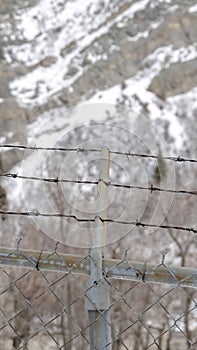 Vertical crop Focus on security chain link fence with barbed wires against on snowy hill slope