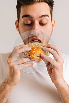 Vertical cropped shot of hungry young man with enjoying eating delicious burger on white  background.